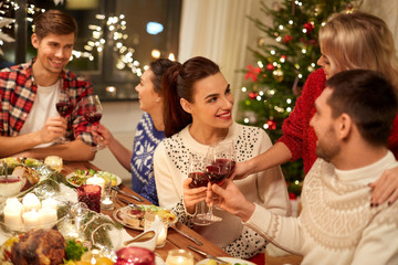 holidays and celebration concept - happy friends having christmas dinner at home, drinking red wine and clinking glasses