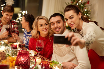 holidays and celebration concept - happy friends having christmas dinner at home and taking selfie by smartphone