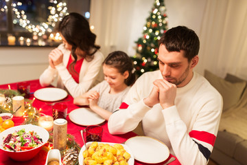 holidays, family and celebration concept - happy mother, father and little daughter having christmas dinner and praying before meal at home