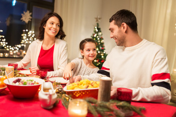 holidays, family and celebration concept - happy mother, father and little daughter having christmas dinner at home