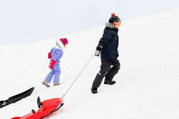 childhood, sledging and season concept - little kids with sleds climbing snow hill in winter