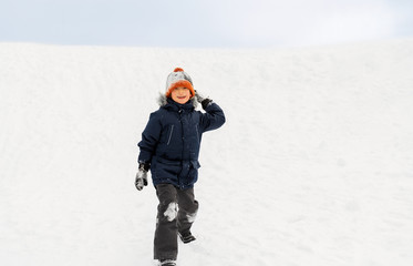 Fototapeta na wymiar childhood, leisure and season concept - happy little boy throwing snowball in winter