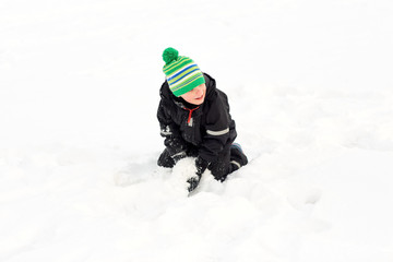 childhood, leisure and season concept - happy little boy playing with snow in winter