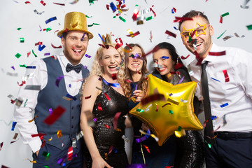 celebration, fun and holidays concept - happy friends with golden party props and confetti laughing