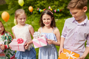 holidays, childhood and celebration concept - happy kids with gifts on birthday party at summer park 