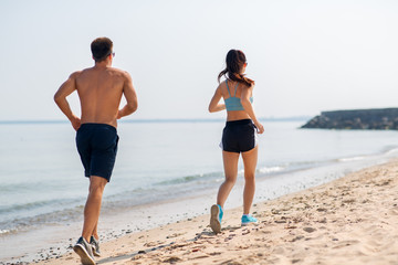 fitness, sport and lifestyle concept - happy couple running along summer beach