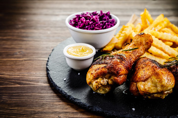 Grilled drumsticks with french fries and vegetables on wooden background
