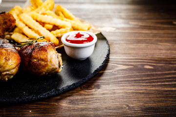 Grilled drumsticks with french fries and vegetables on wooden background