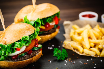 Tasty hamburgers with french fries served on fashionable black stone plate