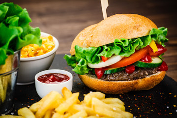Tasty hamburgers with french fries served on fashionable black stone plate