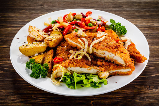 Fried pork chop with potatoes and vegetable salad on wooden background