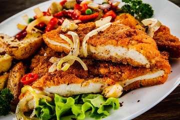 Fried pork chop with potatoes and vegetable salad on wooden background