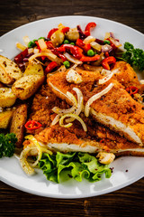 Fried pork chop with potatoes and vegetable salad on wooden background