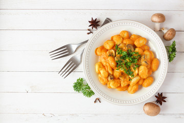 Gnocchi with a pumpkin, mushroom cream sauce. Autumn meal. Top view table scene on a white wood background.