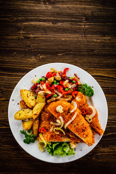 Fried pork chop with potatoes and vegetable salad on wooden background