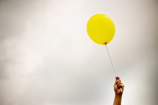 single yellow balloon under cloudy sky. hand holds the balloon rope up to the sky.keep your hope during bad day concept. image for background, wallpaper and copy space.