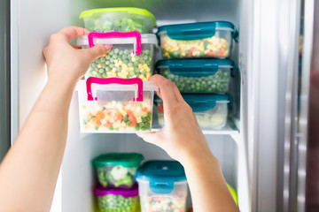 Woman taking container with frozen mixed vegetables from refrigerator.