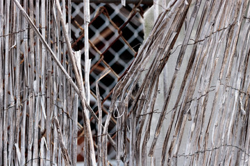 Vintage bamboo rattan close-up of a dilapidated retro worn fence held together with rusted wire,...