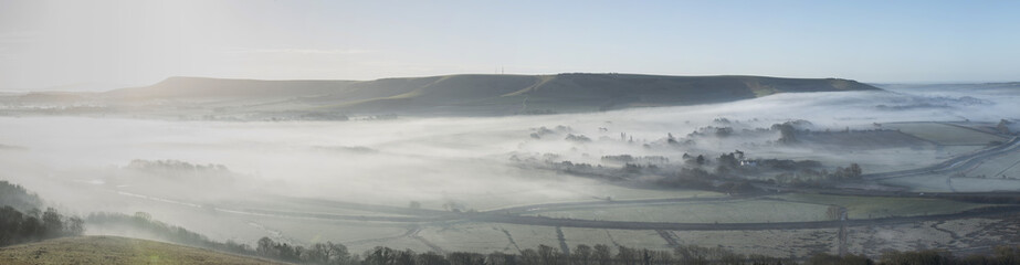 Stunning foggy English rural landscape at sunrise in Winter with layers rolling through the fields