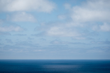 Naklejka na ściany i meble Low ocean horizon below fluffy clouds and blue sky.