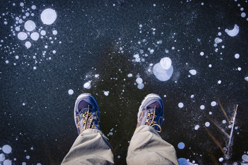 Obraz premium Man wearing hiking boots is standing on a frozen lake, top view