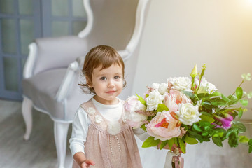 Sweet little girl in pastel pink dress at home play with flowers bouquet, relaxing in white living room. Childhood, preschool, youth, relax concept