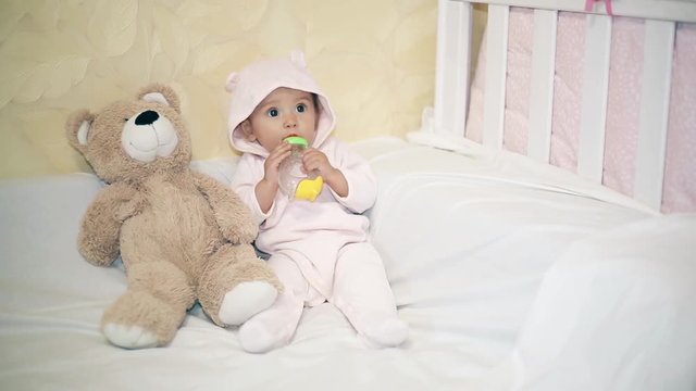 Little baby sitting next to a Teddy bear on a white blanket