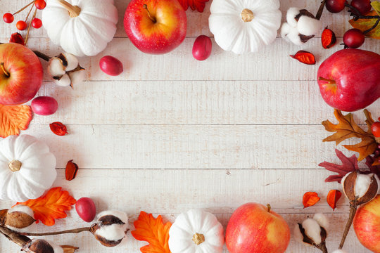 Red and white theme autumn frame with apples and pumpkins on a white wood background. Copy space.