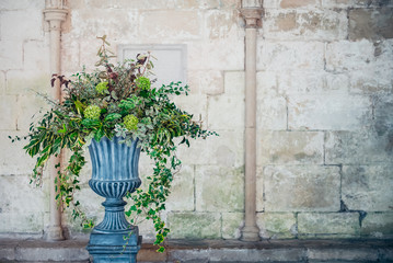 Stone vase planter with fustian green flowers and cascading green ivy and leaves. Grey cobble...