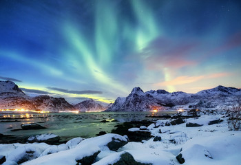 Aurora borealis on the Lofoten islands, Norway. Green northern lights above mountains. Night sky with polar lights. Night winter landscape with aurora and reflection on the water surface. 