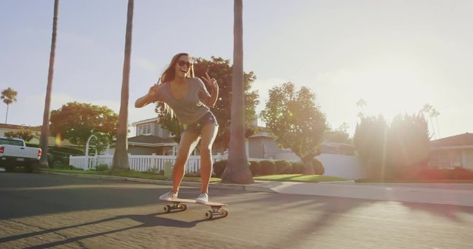 Happy care free girl skateboarding down street at sunset with hands up in air 