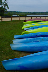 Fototapeta na wymiar Vivid Bright Colorful Kayaks Lined Up In Front of Sandy Blue Beach on a Summer Day