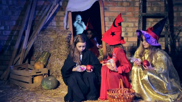 Three girls in witch costumes see a mummy and run away leaving candy. Slow motion.