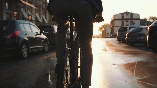 Close up shot of young man driving his bicycle on the street in city center during sunrise in sun beams