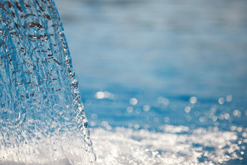 Stream of water in the pool. Blue surface, spray, close-up. Selected focus.