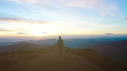 The man standing on the top of the mountain on the sunset background