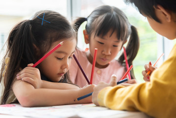 Asian little kids are colouring in a classroom.