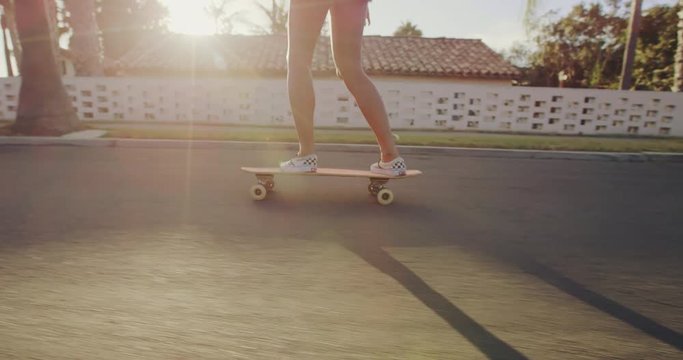 Close up slow motion shot of girls feet riding skateboard at sunset with lens flare