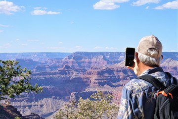 Fototapeta na wymiar A male traveler with backpack taking the photo with smartphone of beautiful view at Grand Canyon National Park, Summer in Arizona USA.