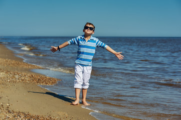 Beautiful boy on a walk by the sea . Trendy baby posing at the seaside