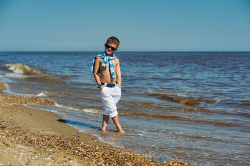 Beautiful boy on a walk by the sea . Trendy baby posing at the seaside