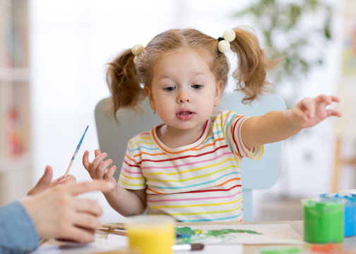 Cute child toddler girl in striped shirt and pony tails paints in the art class