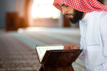 Fototapeta na wymiar Ethnic man reading Koran and praying in mosque