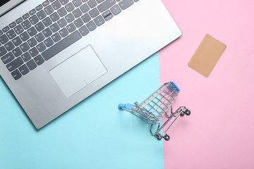 Mini shopping trolley, laptop, credit card on a colored pastel background. The concept of online shopping, top view.