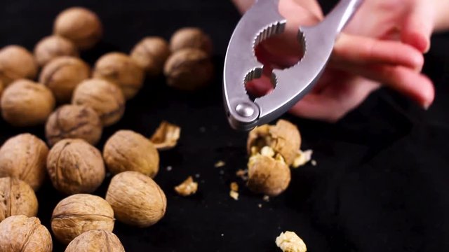 Women's hands crush the walnut on black background. Close up.