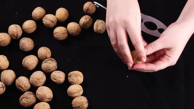 Women's hands crush the walnut on black background. Close up.