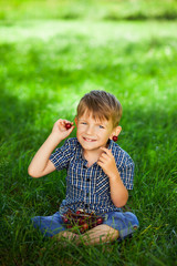 Little boy with cherry on green grass.