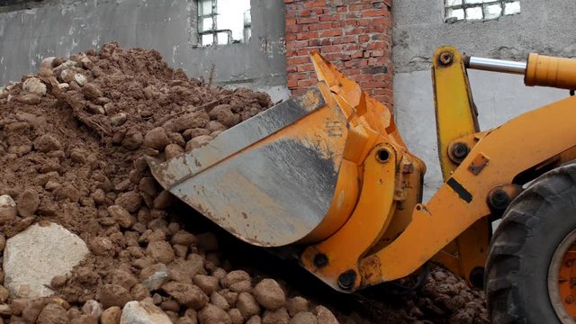 A yellow pusher gathers stones with sand into a sifting bucket, a close-up, loader and stones