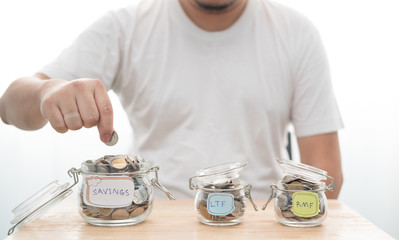 Hand with coin in glass jar saving money. LTF and RMF glass jar with Big glass jar close-up.