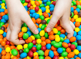 Child's hands taking sweet round candies from the table.